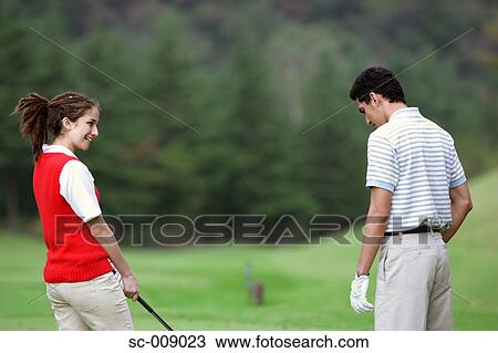 Stock Image - Side view of a couple chatting on the golf course. Fotosearch