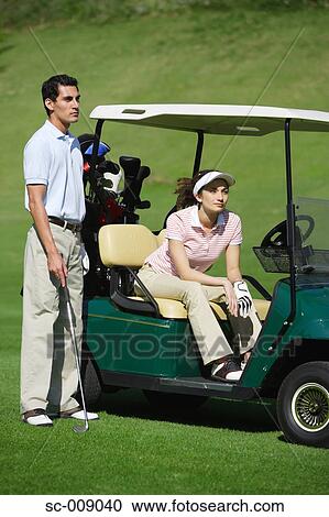 Side view of a woman sitting in a golf cart as a man stands beside her View Large Photo Image Stock Image - Side view of a woman sitting in a golf cart as a man stands beside her. Fotosearch