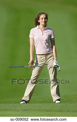 Stock Image - Woman posing in front of the camera holding a golf club. Fotosearch