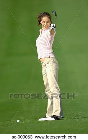 Stock Image - Woman posing in front of the camera holding a golf club. Fotosearch
