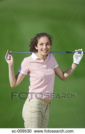 Stock Image - Woman posing in front of the camera holding a golf club. Fotosearch