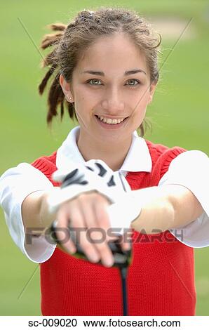 Stock Image - Woman smiling at the camera holding a golf club. Fotosearch