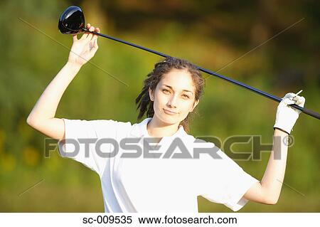 Stock Photography - Woman smiling at the camera while holding a golf club over her head. Fotosearch