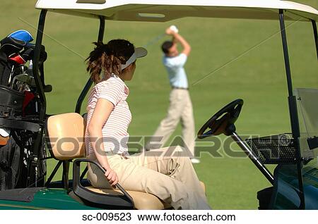 Stock Image - Woman watching her partner play a golf shot. Fotosearch