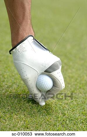Stock Image - Close up of a mans hand teeing a golf ball. Fotosearch
