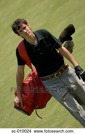 Picture - Front view of a man carrying a red colored golf bag. Fotosearch