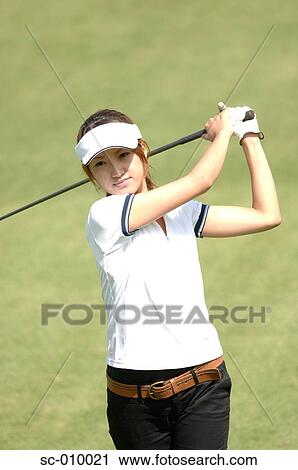 Stock Image - Front view of a woman playing a golf stroke. Fotosearch