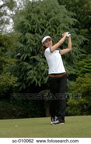 Stock Image - Front view of a woman playing a golf stroke. Fotosearch