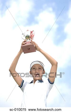 Stock Photography - Low angle view of a woman raising a golf trophy in excitement. Fotosearch
