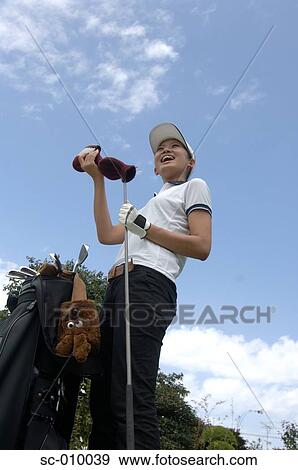 Stock Photo - Low angle view of a woman removing the head cover of a golf club. Fotosearch