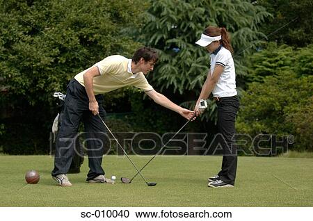 Stock Image - Man teaching a woman to play golf. Fotosearch