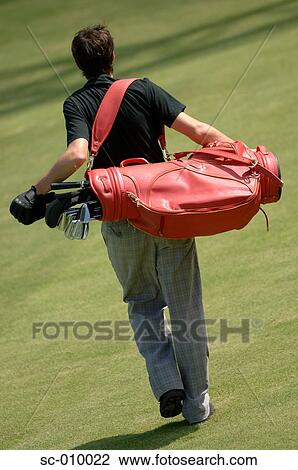 Stock Image - Rear view of a man carrying a red colored golf bag. Fotosearch