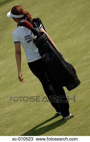 Stock Image - Rear view of a woman carrying a golf bag. Fotosearch