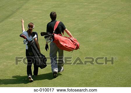 Stock Photo - Rear view of man and a woman carrying their golf bags. Fotosearch