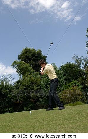 Stock Photo - Side view of a man playing a golf shot. Fotosearch