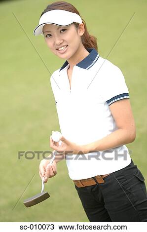 Stock Image - Side view of a woman holding a golf ball and a golf club. Fotosearch