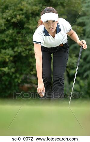 Stock Image - Woman bending to place a golf ball. Fotosearch