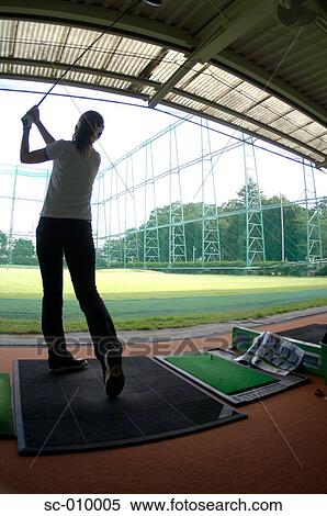 Stock Photography - Woman playing a golf stroke at a golf range. Fotosearch