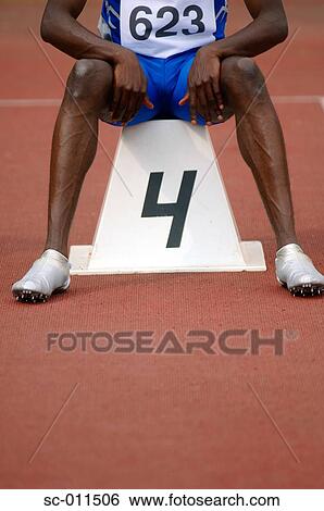 Stock Photograph - Male Runner Sitting on a Starting Block. Fotosearch