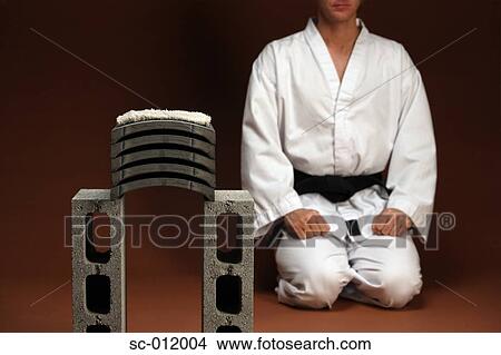 Picture - Blackbelt Kneeling Next To Stack of Concrete. Fotosearch
