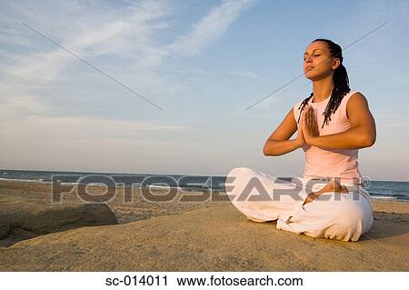 Stock Image - Young woman doing yoga exercises by sea. Fotosearch