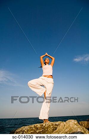 Stock Image - Young woman doing yoga exercises by sea. Fotosearch