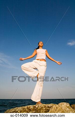 Stock Photo - Young woman doing yoga exercises by sea. Fotosearch