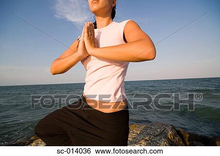 Stock Photograph - Young woman doing yoga exercises by sea. Fotosearch