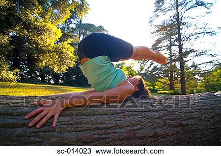 Stock Image - Young woman exercising on tree trunk. Fotosearch