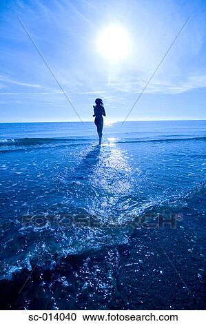 Stock Image - Young woman walking into sea. Fotosearch