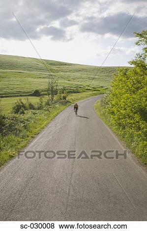 Stock Photo - Cyclist on road through hills. Fotosearch