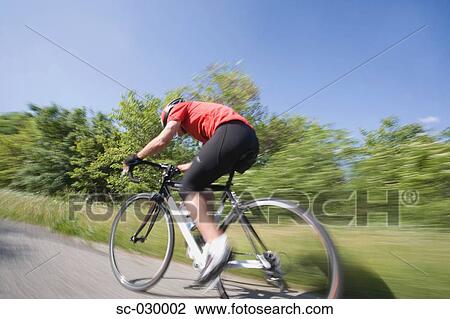 Stock Image - Side view of a cyclist cycling on road, blurred motion. Fotosearch
