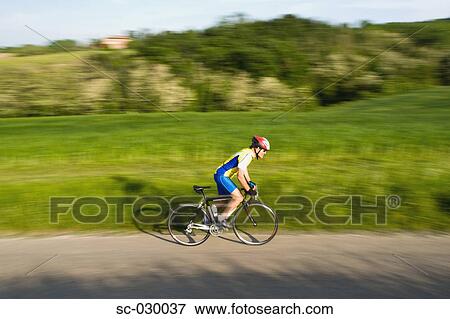 Side view of a man cycling on road View Large Photo Image Stock Photo - Side view of a man cycling on road. Fotosearch