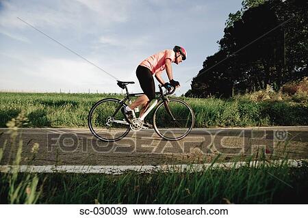 Stock Photo - Side view of a man cycling on road. Fotosearch