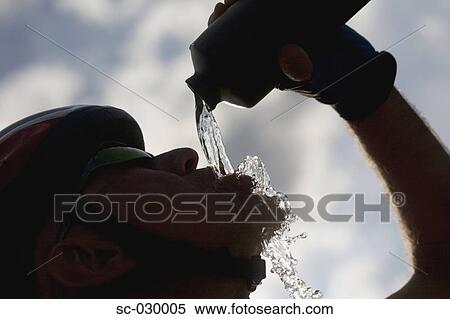 Stock Photography - Silhouetted of a cyclist drinking water, side view. Fotosearch