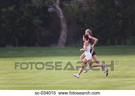 Stock Photography - Two Women Running Together on Grass. Fotosearch