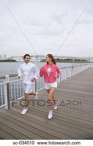 Stock Image - Young couple jogging on bridge. Fotosearch