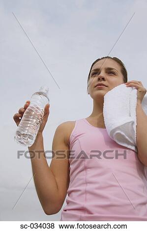 Stock Photo - Young Woman holding water bottle and wiping face with towel. Fotosearch