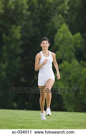 Young Woman in tank top jogging on grass View Large Photo Image Stock Image - Young Woman in tank top jogging on grass. Fotosearch