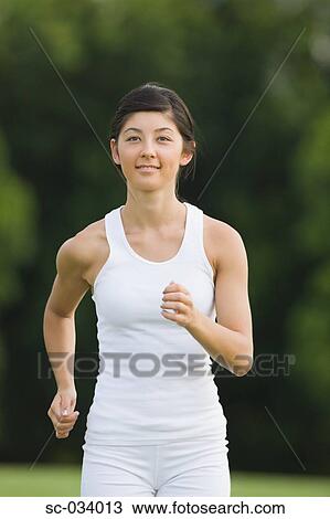 Stock Image - Young Woman in tank top jogging on grass. Fotosearch