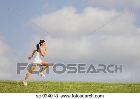 Stock Photo - Young Woman in tank top jogging on grass. Fotosearch