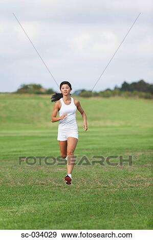 Stock Photo - Young Woman in tank top jogging on grass. Fotosearch