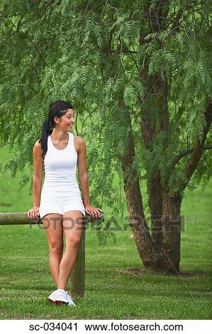 Stock Image - Young Woman sitting on log near tree. Fotosearch