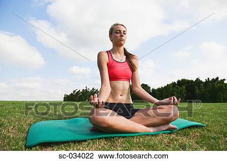 Stock Image - Young Woman sitting on mat in sukhasana position. Fotosearch