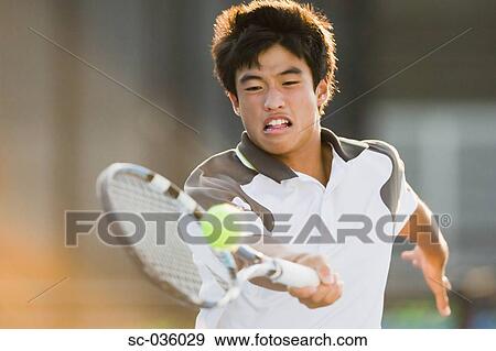 Stock Photo - Young Asian tennis player reaching to hit ball. Fotosearch