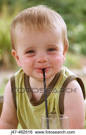 Stock Photograph - 1 year old baby boy smiling cheekily into camera, outside on a sunny day, with a straw in his mouth. Fotosearch