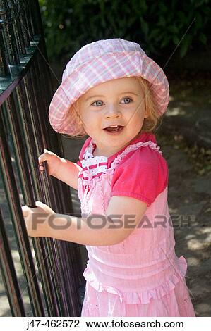 Stock Image - 1 year old girl stanging against a railing inthe park. Fotosearch