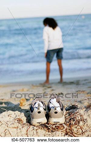 Stock Image - 10-year-old biracial girl at beach, sneakers on sand. Miami, Florida, USA. Fotosearch