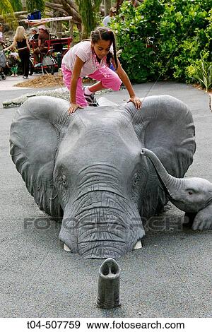 Stock Photo - 10-year-old biracial girl playing on a model elephant. Miami MetroZoo, Miami, Florida, USA. Fotosearch