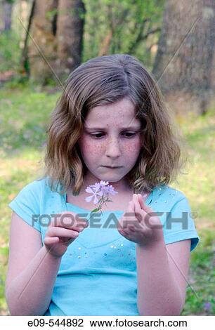 10-year-old girl holding purple wildflower in right hand, petal from flower in left hand, looking a bit concerned, light turquoise short-sleeved shirt with sequins View Large Photo Image Stock Image - 10-year-old girl holding purple wildflower in right hand, petal from flower in left hand, looking a bit concerned, light turquoise short-sleeved shirt with sequins. Fotosearch